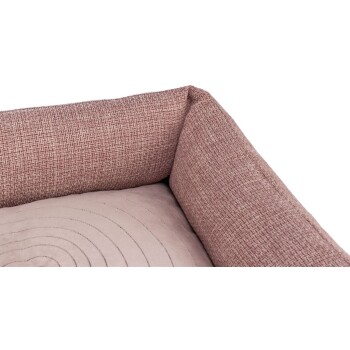 Eine Nahaufnahme eines Haustierbettes mit einem strukturierten rosa Stoffrand und einem weichen, gesteppten beigen Innenraum.