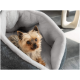 Ein kleiner Yorkshire Terrier mit flauschigem Fell ruht sich in einem gemütlichen, grauen Haustierbett mit einer weichen weißen Innenauskleidung aus und schaut neugierig in die Kamera.