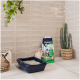 Eine helle Katze sitzt neben einer dunklen Katzentoilette und einem Biokat's Classic 3in1 Katzenstreubeutel, mit einem geflochtenen Korb und einem Kaktus im Hintergrund.