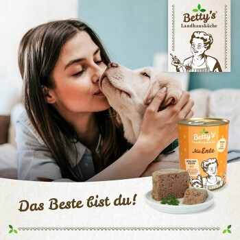Eine Frau interagiert mit einem Hund neben einer Dose Betty's Landhausküche Hundefutter, mit dem Text "Das Beste bist du!" darunter.