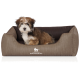 Ein kleiner, flauschiger Welpe sitzt bequem in einem stilvollen braunen Hundebett mit gerippter Textur, mit dem Logo "KNUFFELWUFF."
