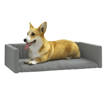 Ein glücklicher Corgi liegt auf einem grauen Haustierbett mit erhöhten Seiten, zeigt seine Zunge und eine entspannte Haltung.