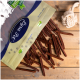 Eine Tüte mit Haustierleckereien mit einem transparenten Deckel, die braune, stäbchenförmige Snacks auf eine Holzoberfläche fallen lässt, neben einem Seilspielzeug.