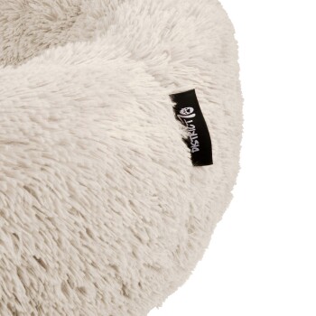 Nahaufnahme eines flauschigen, hellen Haustierbettes mit einem schwarzen Etikett, das den Markennamen "Pawstruck" zeigt.