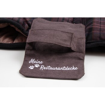Eine Nahaufnahme einer Haustierdecke mit einem braunen Stoffetikett, das in weißer Stickerei "Meine Restaurantdecke" liest, mit Pfotenabdrücken.