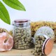 Zwei Glasbehälter mit Haustierfutterpellets, einer umgekippt und auf Holz verschüttet, mit einem rosa Salzkristall und Stroh im Hintergrund.