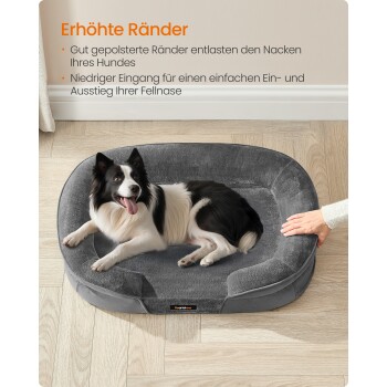 Schwarz-weißer Hund liegt auf einem grauen Hundebett mit erhöhtem Rand, eine Hand berührt die Seite des Bettes.