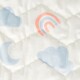 A close-up of a soft, quilted fabric featuring a playful design with light blue clouds, a crescent moon, and a pastel rainbow.