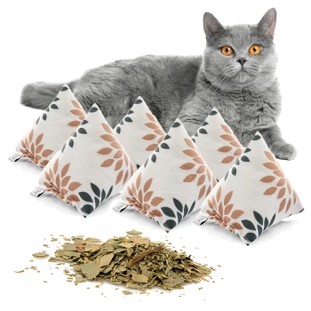 Eine graue Katze mit leuchtend orangefarbenen Augen liegt hinter fünf dekorativen Kissen, gefüllt mit Katzenminze und mit Blattmustern, und getrocknete Katzenminze ist davor verstreut.