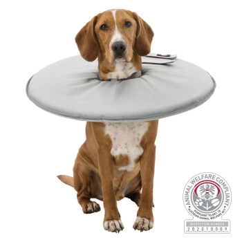 Ein Hund mit einem weichen, grauen Schutzkragen sitzt aufrecht. Das Bild enthält ein Tierschutzkonformitätsabzeichen in der unteren rechten Ecke.