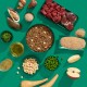 Flachansicht von Haustierfutterzutaten: Nassfutter mit Erbsen und Apfel, rohem Fleisch, Käse, Quinoa, Pastinake und Algen auf einem türkisfarbenen Hintergrund.