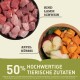 Schüssel mit rohen Fleischwürfeln (Rind, Lamm, Schwein) neben einem Teller mit Apfel und Kürbis, mit dem Text '50% hochwertige tierische Zutaten.'