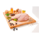 Ein Holzschneidebrett hält eine rohe Hähnchenbrust mit grünen Erbsen, Heidelbeeren, Apfelscheiben, Ingwer, Pilzen und einem Glas Öl.
