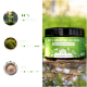 Ein Glas mit "Kot & Grasfrei Leckerli" Hundefutterergänzung, 100% natürlich mit Naturmoor und Flohsamen, auf einem grünen Pflanzenhintergrund.