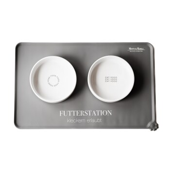 Graue Futtermatte mit zwei weißen Schalen, beschriftet mit "CAT FOOD" und "FOOD," mit "FUTTERSTATION" und "kleckern erlaubt."