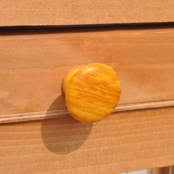 Nahaufnahme eines runden, gelben Schubladengriffes an einer Holzschublade, der seine glatte Textur und helle Farbe zeigt.