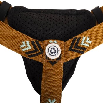 Nahaufnahme eines Hundegeschirrs mit schwarzem Netzinnenfutter, braunem Riemen, türkisfarbenen und schwarzen Zickzackmustern sowie einem Etikett, das "Recyceltes Glas" sagt.