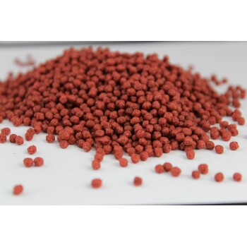 Nahaufnahme eines Haufens kleiner, runder, rötlich-brauner Haustierfutterpellets, die auf einer weißen Oberfläche verstreut sind.