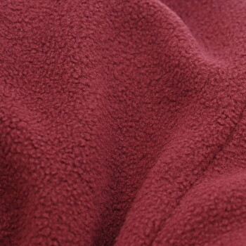 Gestromter Hund trägt eine dunkelrote Fleece-Weste mit schwarzem Besatz, sitzt vor weißem Hintergrund.