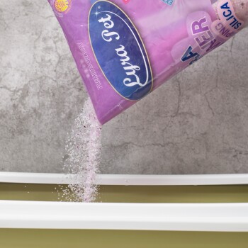 Eine Tüte Lyra Pet Katzenstreu in Premium-Qualität wird ausgegossen, wobei rosa und weiße Granulate in eine weiße Katzentoilette fallen.