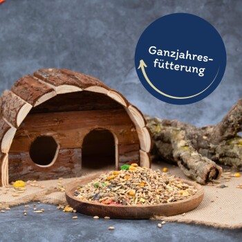 Ein Holzhaustierhaus neben einer Schüssel mit buntem Haustierfutter, mit dem Text "Ganzjahresfütterung" in einem kreisförmigen Design darüber.