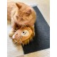 Eine orange getigerte Katze liegt auf einem strukturierten Teppich und ruht neben einem plüschigen Löwen-Spielzeug mit einem lächelnden Gesicht und einer flauschigen Mähne.