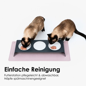 Zwei Siamkatzen fressen aus einem erhöhten Dreifachnapf auf einer rosa Matte; sichtbarer Text: 'Einfache Reinigung.'