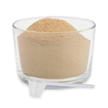 Ein Glasbehälter gefüllt mit hellbraunem Pulver, mit einem kleinen Messlöffel, der an der Seite lehnt.