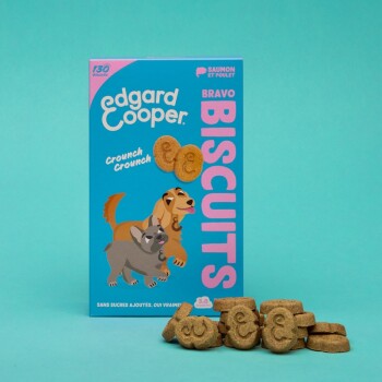 Boîte de biscuits Edgard Cooper Bravo avec des chiens de dessin animé, avec le texte "Crunch Crunch" et "130 Biscuits," accompagnée de friandises en forme de chien.