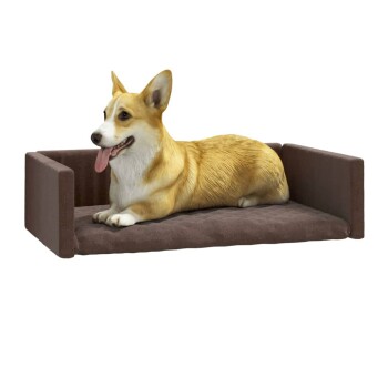 Ein entspannter Corgi, der auf einem plüschigen braunen Hundebett mit erhöhten Seiten liegt, zeigt seinen glücklichen Ausdruck und die Zunge heraus.