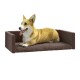 Ein entspannter Corgi, der auf einem plüschigen braunen Hundebett mit erhöhten Seiten liegt, zeigt seinen glücklichen Ausdruck und die Zunge heraus.