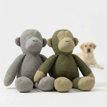 Zwei Stoff-Affenplüschtiere, eines olivgrün und beige, eines grau, mit einer Baumwollpflanze in einem Topf dahinter.