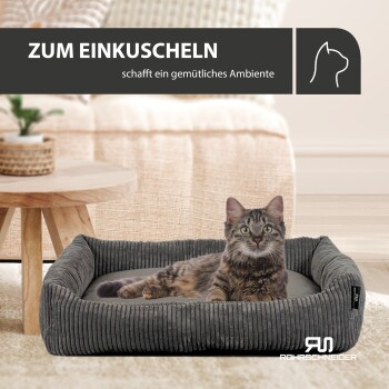 Ein graues Haustierbett mit einer liegenden getigerten Katze, einem Holztisch und einer Pflanze. Text: "ZUM EINKUSCHELN schafft ein gemütliches Ambiente."