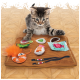 Un chaton tabby joueur interagit avec un tapis de sushi en feutre coloré comportant des articles en peluche sushi, y compris des crevettes, du poisson et des baguettes.