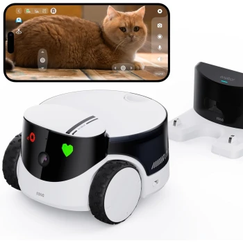 Eine weiß-schwarze Roboter-Haustierkamera mit einem Herzaufkleber steht neben ihrer Ladestation, neben einem Smartphone, das eine flauschige orangefarbene Katze zeigt.