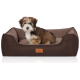 Flauschiger braun-weißer Welpe, der in einem rechteckigen braunen Hundebett mit Lederaufnäher mit der Aufschrift KNUFFELWUFF sitzt.