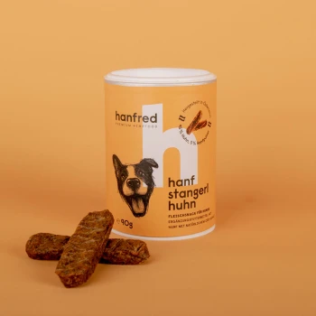 Ein Behälter mit "hanfred" Premium Hanf-Futter für Hunde, beschriftet "hanf stangerl huhn," mit drei braunen Hundeleckerlis davor.