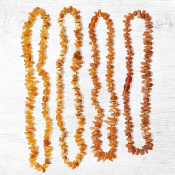 Vier Stränge von bernsteinfarbenen Haustierhalsbändern aus polierten Steinen, auf einem hellen Holzuntergrund präsentiert.