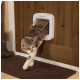 Eine getigerte Katze verlässt eine PetSafe-Katzentür, die in eine Holztür eingebaut ist, mit einem braunen Fußmatte sichtbar darunter.