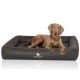 Ein brauner Hund liegt auf einem plüschigen, dunkelgrauen Hundebett mit gesticktem Rand, das das Logo "KNUFFELWUFF" zeigt.