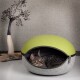 Eine getigerte Katze entspannt sich in einem gemütlichen, modernen Haustierbett mit einem grünen Oberteil und grauem Boden, vor einem neutralen Hintergrund.