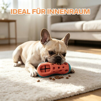 Französische Bulldogge kaut an einem orangefarbenen Leckerli-Spielzeug auf einem Teppich mit Trockenfutter; sichtbarer Text 'IDEAL FÜR INNENRAUM'.