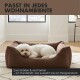 Weißer Hund zusammengerollt in braunem Designer-Hundebett in hellem Raum; sichtbarer deutscher Text: 'PASST IN JEDES WOHNAMBIENTE'.