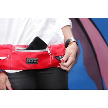 Eine Frau in einem weißen Hemd und schwarzen Hosen hält eine rote DOOG-Hüfttasche mit einem Smartphone in der vorderen Tasche.