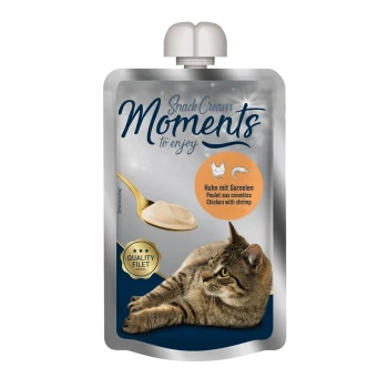 Pouch of cat snack cream labeled "Moments to enjoy," featuring chicken with shrimp, with a spoon and a cat lying beside it.