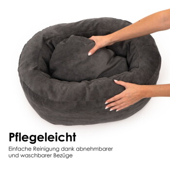 Graues Cord-Rundbett mit herausnehmbarem Kissen, das von Händen gerichtet wird; sichtbarer Text „Pflegeleicht“ und deutscher Pflegehinweis.