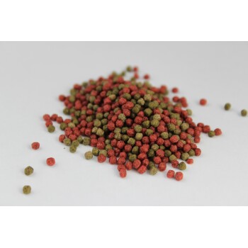 Ein Haufen kleiner, runder Haustierfutterpellets in Rot- und Grüntönen auf einem weißen Hintergrund.