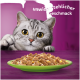 Grijs gestreepte kat gluurt over de tafel naar een groen bord met kattenvoer, paarse achtergrond met tekst 'unwiderstehlicher Geschmack'
