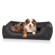 Ein glücklicher Australian Shepherd Hund, der in einem stilvollen schwarzen Haustierbett mit einem Lederetikett, das 'KNUFFELWUFF' liest, entspannt.