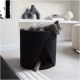 Eine flauschige graue Katze, die in einem schwarzen, strukturierten Haustierbett mit einer offenen Seite entspannt, in einem modernen Wohnzimmer.